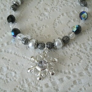 May include: A silver snowflake charm necklace with black, white, and iridescent beads.