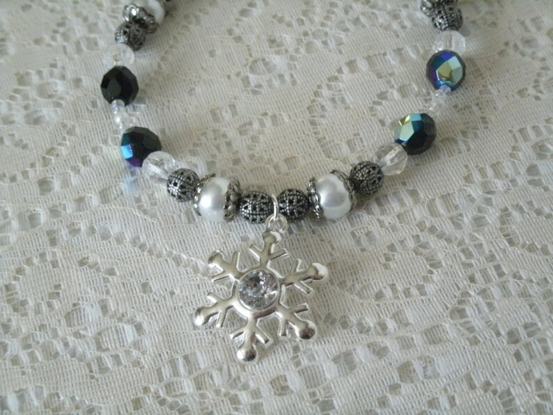 May include: A silver snowflake charm necklace with black, white, and iridescent beads.