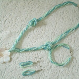May include: A set of blue and white beaded jewelry, including a necklace, bracelet, and earrings. The necklace features a large, white shell flower pendant.