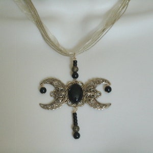 Puede incluir: Collar con colgante plateado con un dise&ntilde;o de triple luna y una gran piedra negra ovalada en el centro. Las medias lunas tienen intrincados patrones de filigrana y cuentas negras. La cadena es delicada, transparente y similar a una cinta.