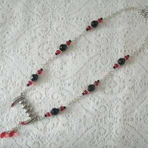 May include: A silver chain necklace with black and red beads and a silver fang pendant.