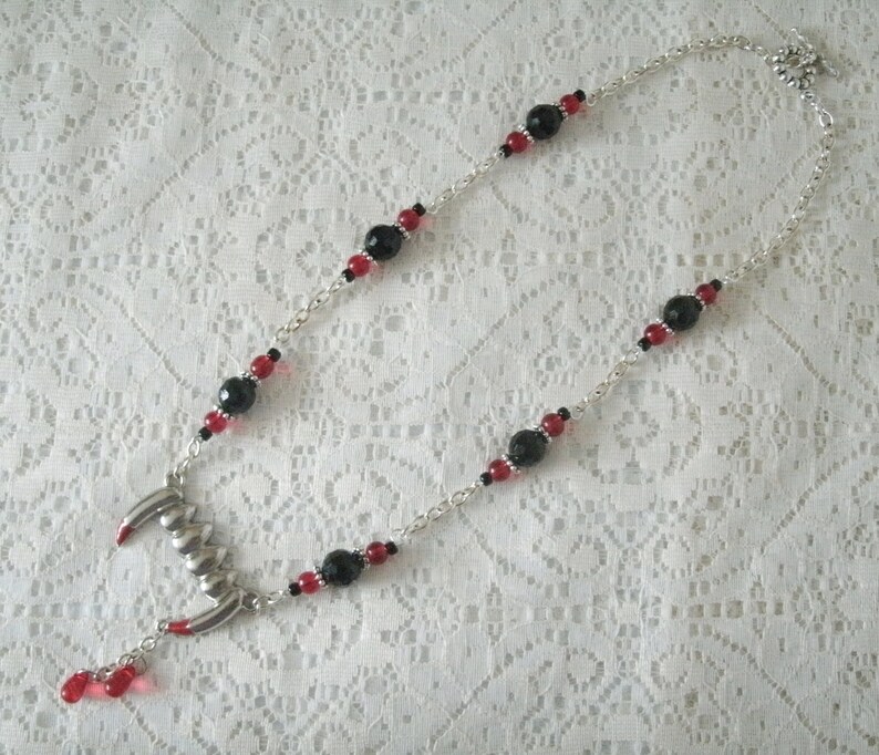 May include: A silver chain necklace with black and red beads and a silver fang pendant.