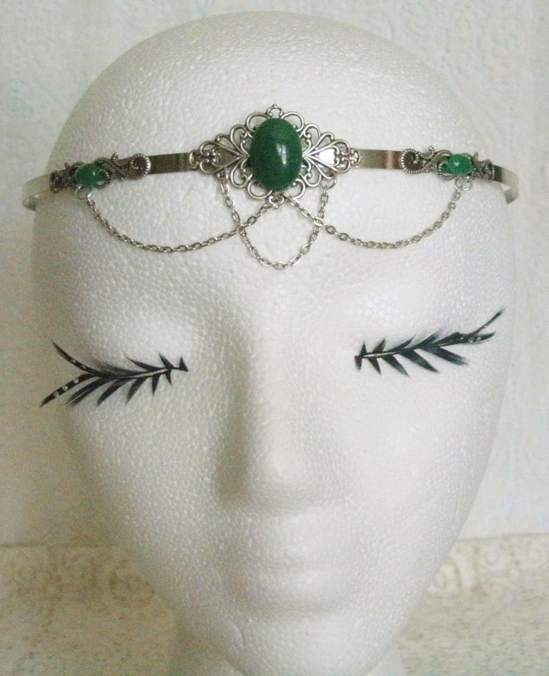 May include: Silver headband with a green gemstone and smaller green stones on the sides. The headband has a delicate chain design.