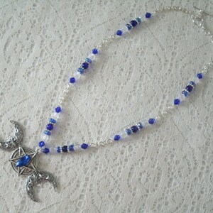 May include: A silver triple moon necklace with a blue crystal in the centre. The necklace is made with silver chain and blue and clear glass beads.