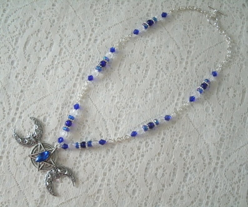 May include: A silver triple moon necklace with a blue crystal in the centre. The necklace is made with silver chain and blue and clear glass beads.
