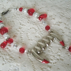 May include: A silver claw pendant necklace with red and white beads. The necklace is made with silver metal and has a red enamel finish on the claw.