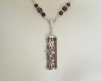 Puede incluir: Un collar de plata con una cadena de cuentas de vidrio morado y un colgante con forma de cilindro de plata con una piedra morada y un diseño de estrella de plata.