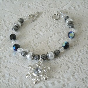 May include: A silver bracelet with black, white, and iridescent blue beads, and a silver snowflake charm.
