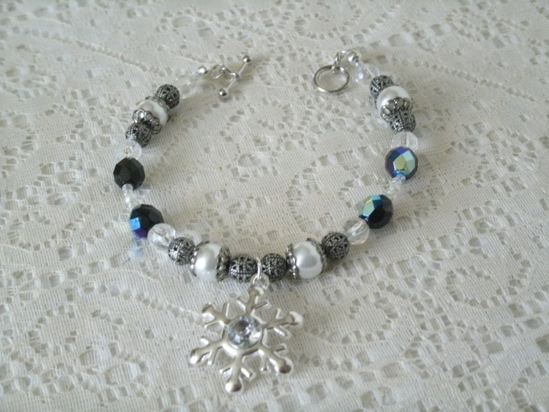 May include: A silver bracelet with black, white, and iridescent blue beads, and a silver snowflake charm.