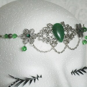 Puede incluir: Diadema de plata con una piedra preciosa verde, cuentas de vidrio verde y detalles florales plateados.