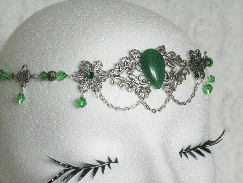 Puede incluir: Diadema de plata con una piedra preciosa verde, cuentas de vidrio verde y detalles florales plateados.