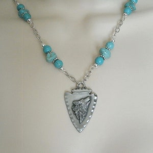 May include: A silver necklace with a turquoise bead chain and a silver arrowhead pendant with a wolf head design.