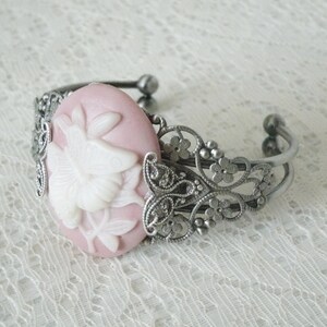 May include: A silver filigree bracelet with a pink cameo featuring a white floral design.