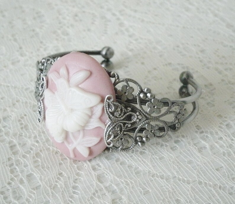 May include: A silver filigree bracelet with a pink cameo featuring a white floral design.