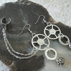 May include: A pair of silver earrings with a chain and a cuff. The earrings feature a circular design with a small bead at the end. The cuff is a simple band with a chain attached.