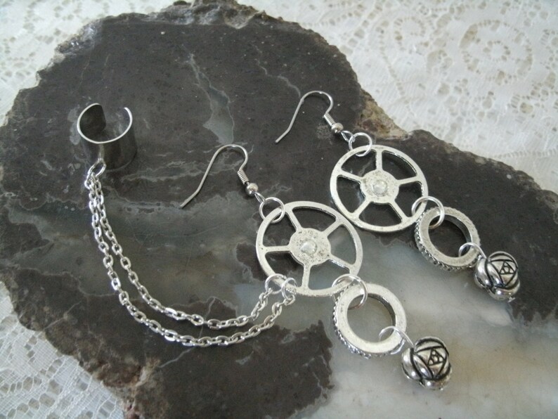 May include: A pair of silver earrings with a chain and a cuff. The earrings feature a circular design with a small bead at the end. The cuff is a simple band with a chain attached.