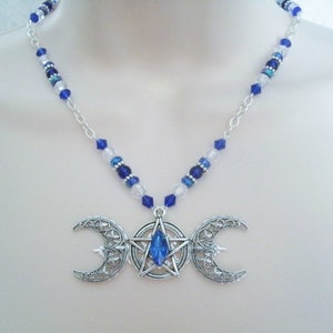May include: A silver triple moon necklace with a blue crystal in the centre of the pentacle. The necklace is made with silver chain and blue and clear glass beads.