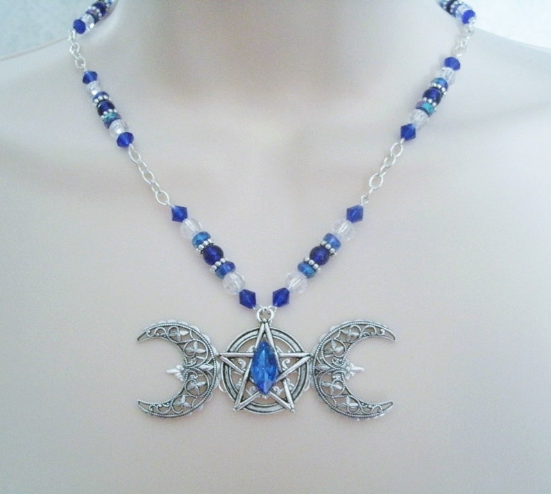 May include: A silver triple moon necklace with a blue crystal in the centre of the pentacle. The necklace is made with silver chain and blue and clear glass beads.
