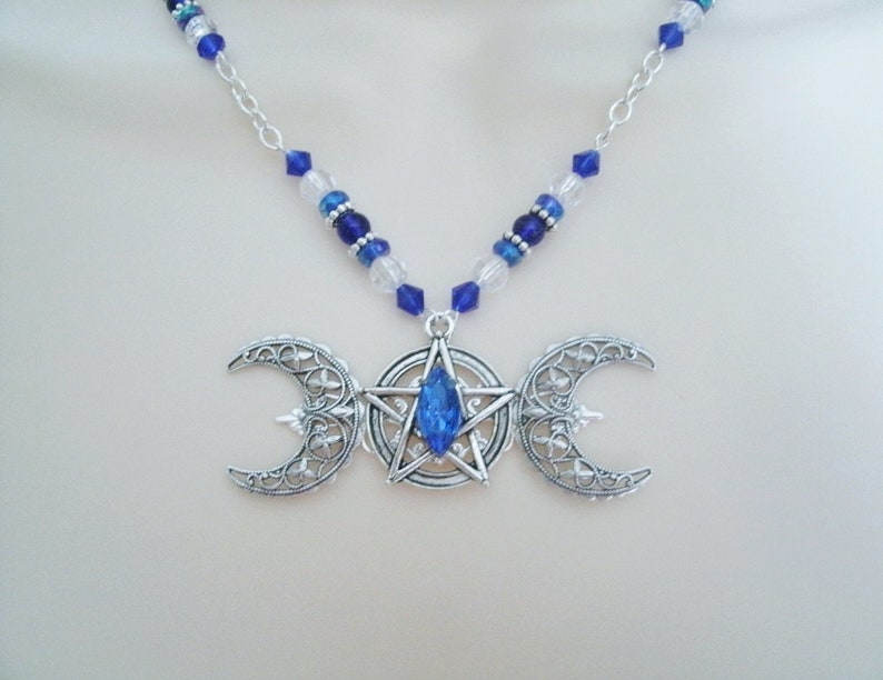 May include: A silver necklace with a triple moon pendant featuring a blue crystal star in the centre. The necklace is made with blue and clear glass beads.