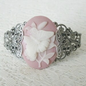 May include: A silver filigree bracelet with a pink cameo featuring a white butterfly design.