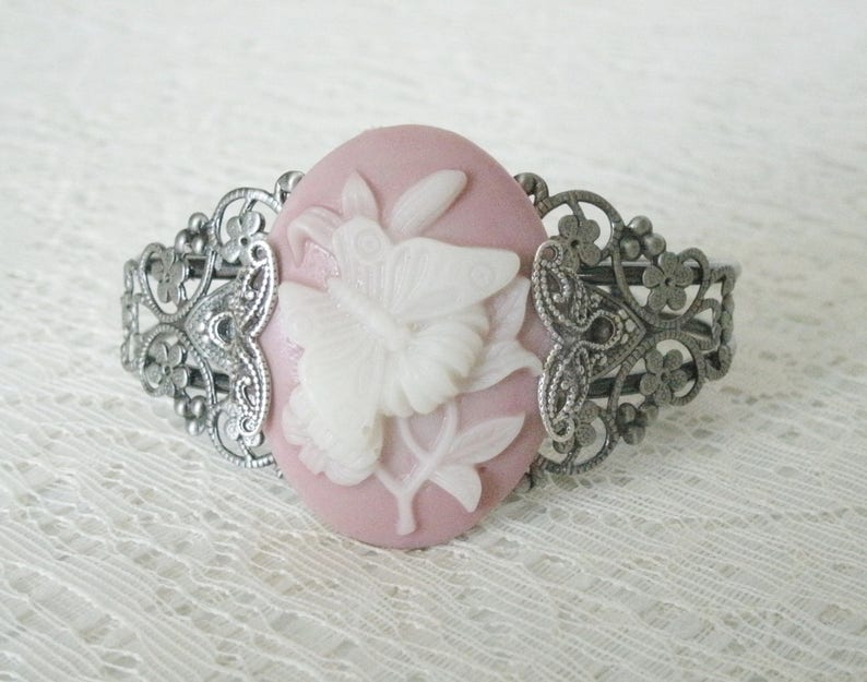 May include: A silver filigree bracelet with a pink cameo featuring a white butterfly design.
