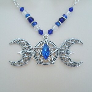 May include: A silver necklace featuring a triple moon pendant with a blue crystal at the centre of a pentagram. The necklace is made with blue and clear glass beads.