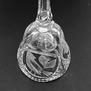 Op de afbeelding: Transparante glazen bel met een facetgeslepen handvat en een gedetailleerd, geëtst ontwerp. De bel heeft een vogel- en bladerenmotief, met ingewikkelde sneden en patronen. Een decoratief stuk.