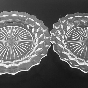 K&ouml;nnte beinhalten: Zwei klare Glasplatten mit einem rautenf&ouml;rmigen Muster an den R&auml;ndern und einem Sonnenstrahl-Design in der Mitte. Die Teller haben einen gewellten Rand und sind zum Servieren von Speisen oder zur Pr&auml;sentation geeignet.