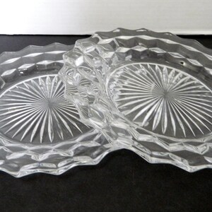 K&ouml;nnte beinhalten: Zwei ovale Teller aus klarem Glas. Jeder Teller hat ein Diamantmuster am Rand und ein Sonnenstrahl-Design in der Mitte. Die Teller bestehen aus klarem Glas und liegen auf einer dunklen Oberfl&auml;che.