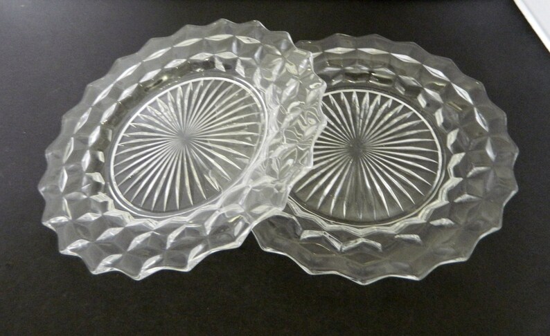 K&ouml;nnte beinhalten: Zwei klare Glasplatten mit einem rautenf&ouml;rmigen Muster an den R&auml;ndern. Die Mitte jeder Platte weist ein Sonnenstrahl-Design auf. Die Platten bestehen aus klarem Glas.