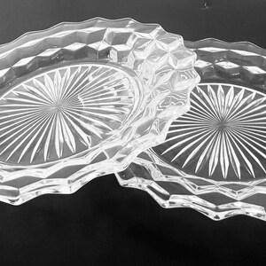 K&ouml;nnte beinhalten: Zwei ovale Schalen aus klarem Glas. Jede Schale hat ein rautenf&ouml;rmiges Muster am Rand und ein Sonnenstrahl-Design in der Mitte. Die Schalen befinden sich auf einer dunklen Oberfl&auml;che.