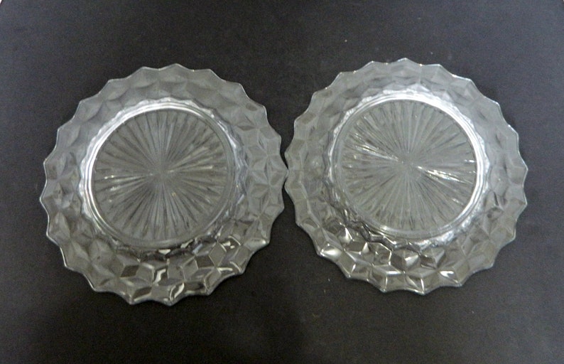 K&ouml;nnte beinhalten: Zwei klare Glasplatten mit einem strukturierten, geometrischen Design am Rand und einem radialen Muster in der Mitte. Die runden Teller eignen sich zum Servieren von Speisen oder als dekorative Elemente.