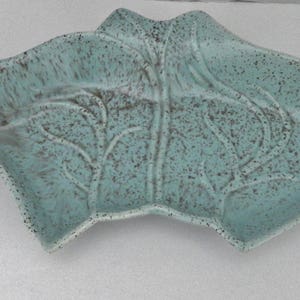 Puede incluir: Un plato de cerámica turquesa con forma de hoja y acabado moteado. El plato tiene un diseño detallado de venas de hoja y un borde ligeramente elevado. Ideal para servir o exhibir.