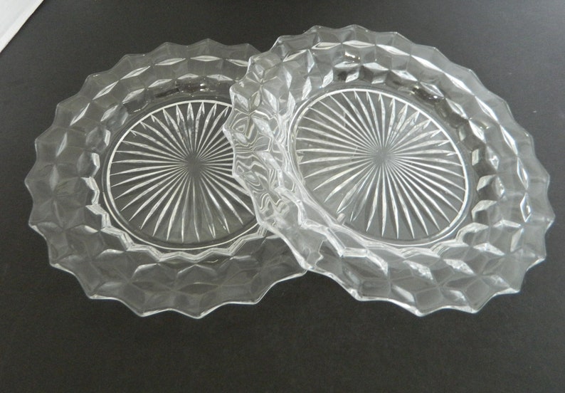 K&ouml;nnte beinhalten: Zwei Servierschalen aus klarem Glas. Jede Schale hat einen gewellten Rand und ein Rautenmuster am Rand. Die Mitte jeder Schale weist ein Sternmuster auf. Die Schalen sind durch einen Griff verbunden.