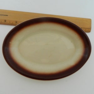 Könnte beinhalten: Eine ovale Keramikschale mit cremefarbenem Innenraum und dunkelbraunem Rand. Ein Holzlineal liegt in der Nähe der Schale. Die Schale ist etwa 20 cm lang.