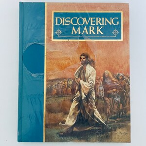 Peut inclure: Un livre à couverture rigide intitulé "Discovering Mark" avec un dos bleu et une étiquette dorée. La couverture présente une peinture d'une figure en robes blanches marchant vers une foule, sur fond de paysage aux couleurs chaudes et terreuses.