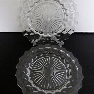 K&ouml;nnte beinhalten: Zwei klare Glasplatten mit einem Diamantmuster an den R&auml;ndern und einem Sonnenstrahl-Design in der Mitte. Die Teller werden auf einer schwarzen Oberfl&auml;che mit wei&szlig;em Hintergrund pr&auml;sentiert.