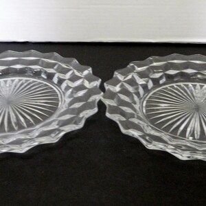 K&ouml;nnte beinhalten: Zwei ovale Schalen aus klarem Glas. Jede Schale hat einen rautenf&ouml;rmigen Rand und eine Mitte mit einem Sonnenstrahl-Design. Die Schalen werden auf einer dunklen Oberfl&auml;che pr&auml;sentiert.