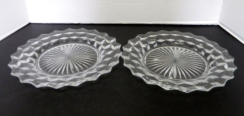 K&ouml;nnte beinhalten: Zwei ovale Schalen aus klarem Glas. Jede Schale hat einen rautenf&ouml;rmigen Rand und eine Mitte mit einem Sonnenstrahl-Design. Die Schalen werden auf einer dunklen Oberfl&auml;che pr&auml;sentiert.