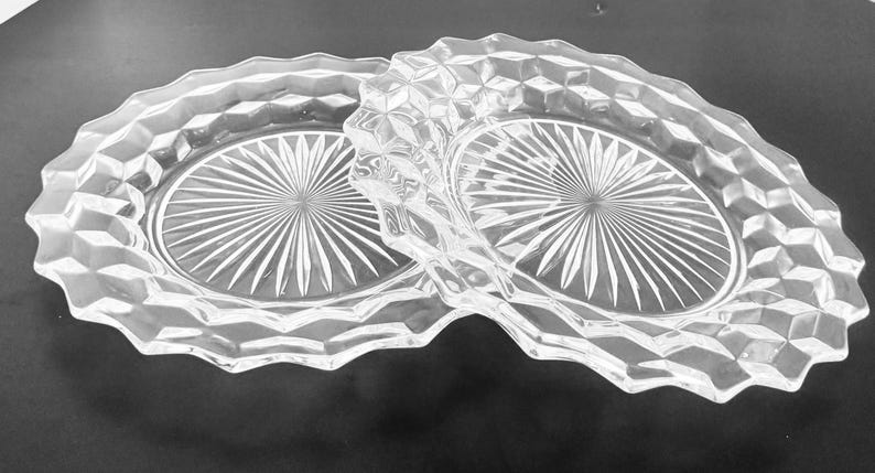K&ouml;nnte beinhalten: Klarer Servierteller aus Glas mit zwei ovalen F&auml;chern. Der Teller hat ein rautenf&ouml;rmiges Muster an den R&auml;ndern und ein Sternmuster in der Mitte jedes Fachs. Der Griff ist ebenfalls rautenf&ouml;rmig.