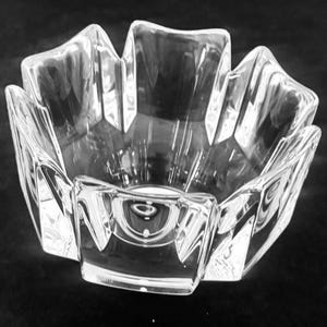 May include: A clear, faceted glass bowl with a starburst design. The bowl has a unique shape with multiple points extending outwards. The glass is transparent, suitable for decorative use. The bowl's dimensions are approximately 15 cm in diameter.