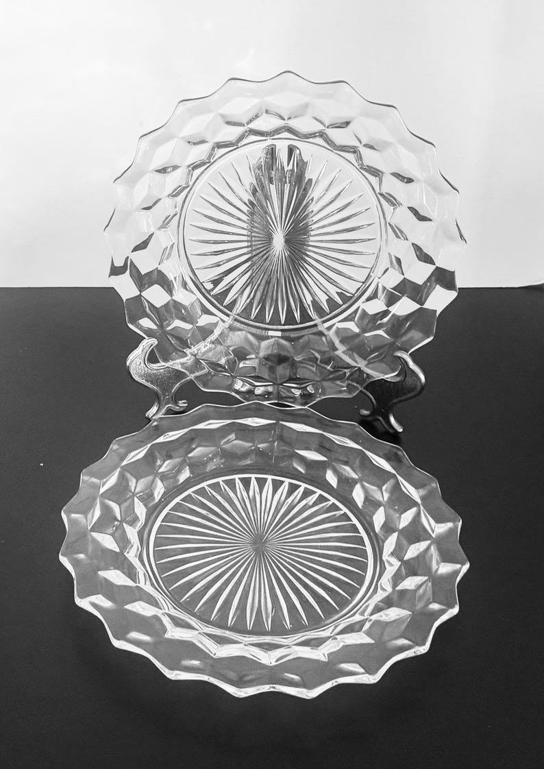 K&ouml;nnte beinhalten: Zwei klare Glasplatten mit rautenf&ouml;rmigen Kanten und einem Sternmuster in der Mitte. Die Teller werden auf einem dekorativen Metallst&auml;nder pr&auml;sentiert, der ihre komplizierten Details und ihr elegantes Design zeigt.