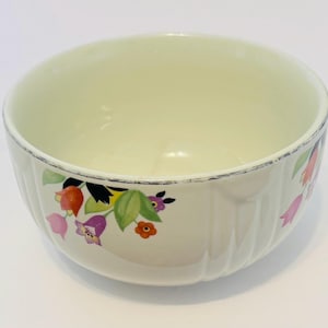 May include: Cream-colored ceramic bowl with a floral design. The bowl features a ribbed exterior and a silver rim. The floral pattern includes red, pink, purple, and orange flowers with green leaves.