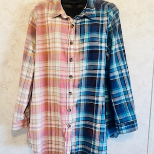 May include: A long-sleeved flannel shirt with a distinctive colour-block design. One side features pink and orange plaid, while the other showcases blue and teal plaid. The shirt has a button-down front and a classic collar.