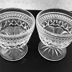 May include: Two clear glass dessert bowls with intricate diamond and starburst patterns. The bowls have a rounded shape with a pedestal base. The glass has a textured, cut-glass appearance, adding to their vintage charm.
