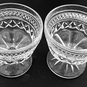 May include: Two clear, vintage-style glass dessert bowls. Each bowl features a decorative diamond and star pattern around the rim and base. The bowls are elevated on a short, stemmed foot.