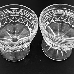 May include: Two clear glass dessert bowls with a decorative diamond and starburst pattern. The bowls have a pedestal base and a wide rim with a repeating geometric design. The bowls are likely vintage and suitable for serving ice cream or other desserts.