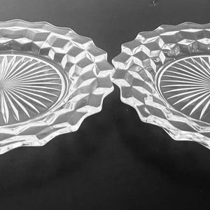 K&ouml;nnte beinhalten: Zwei klare Glasplatten mit einem Sternmuster in der Mitte und einem rautenf&ouml;rmigen Rand. Die Teller haben einen gewellten Rand und werden auf einer dunklen Oberfl&auml;che pr&auml;sentiert.