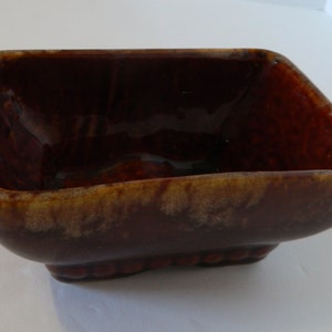 May include: A rectangular, glazed ceramic bowl in a deep brown hue with a glossy finish. The bowl features rounded corners and a textured base, ideal for serving or display.