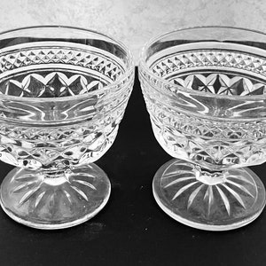 May include: Two clear glass dessert bowls with intricate diamond and starburst patterns. The bowls have a wide, decorative rim and sit on a stemmed base. The glass has a classic, elegant design, suitable for serving desserts.